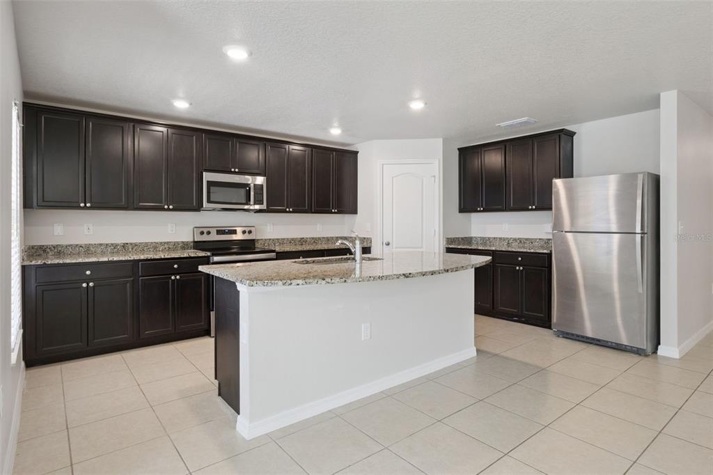 A kitchen features dark wood cabinets, granite countertops, stainless steel appliances, and a central island — 12023 INDIAN GRASS WAY, LEESBURG, FL