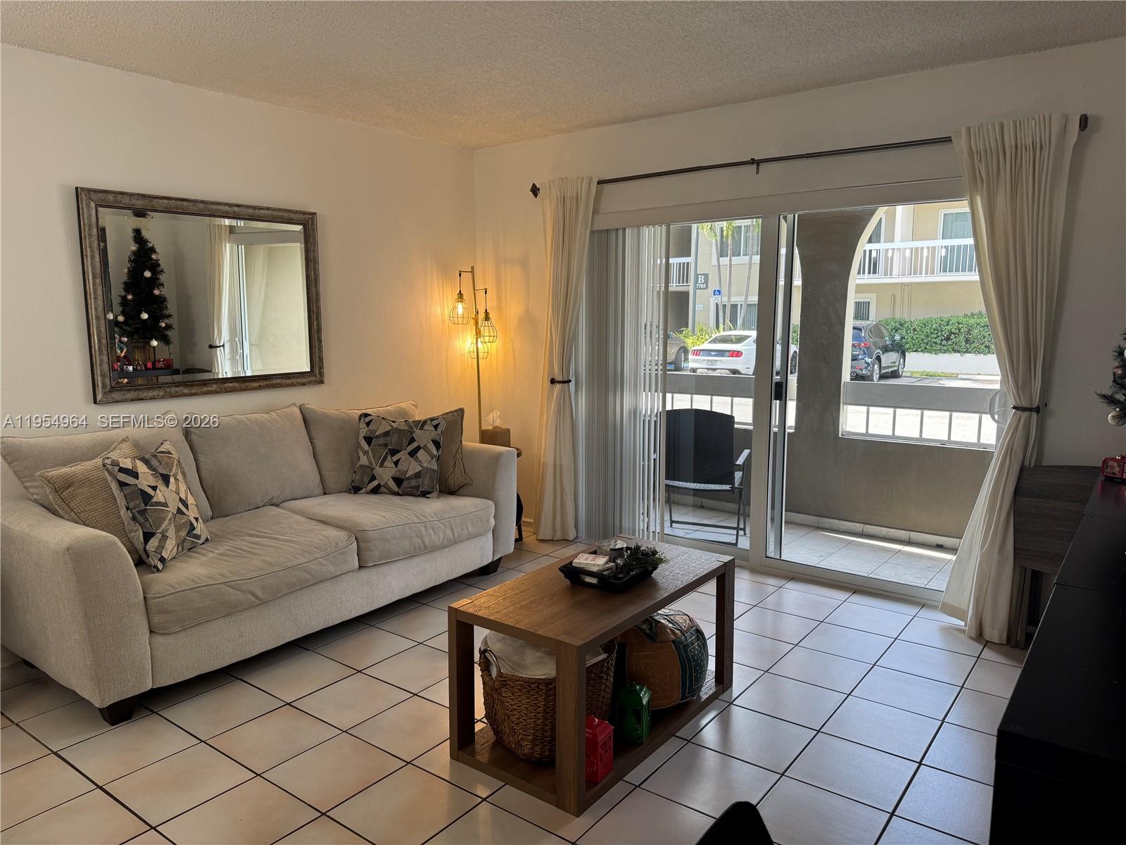 A living room features a beige sofa, wooden coffee table, and sliding glass doors to a balcony — 7703 Camino Real # A106, Miami FL 33143, MIAMI, FL