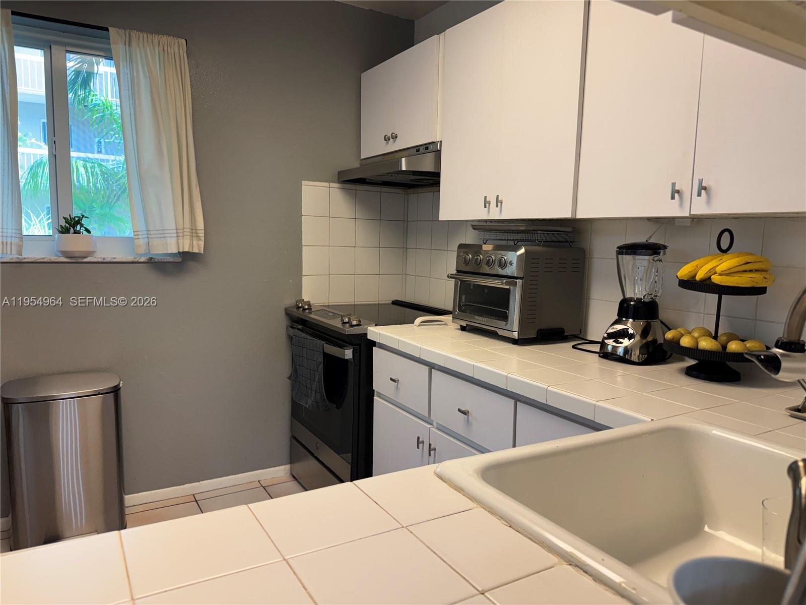 A kitchen features white cabinets, tiled countertops, a stainless steel oven, and a window — 7703 Camino Real # A106, Miami FL 33143, MIAMI, FL