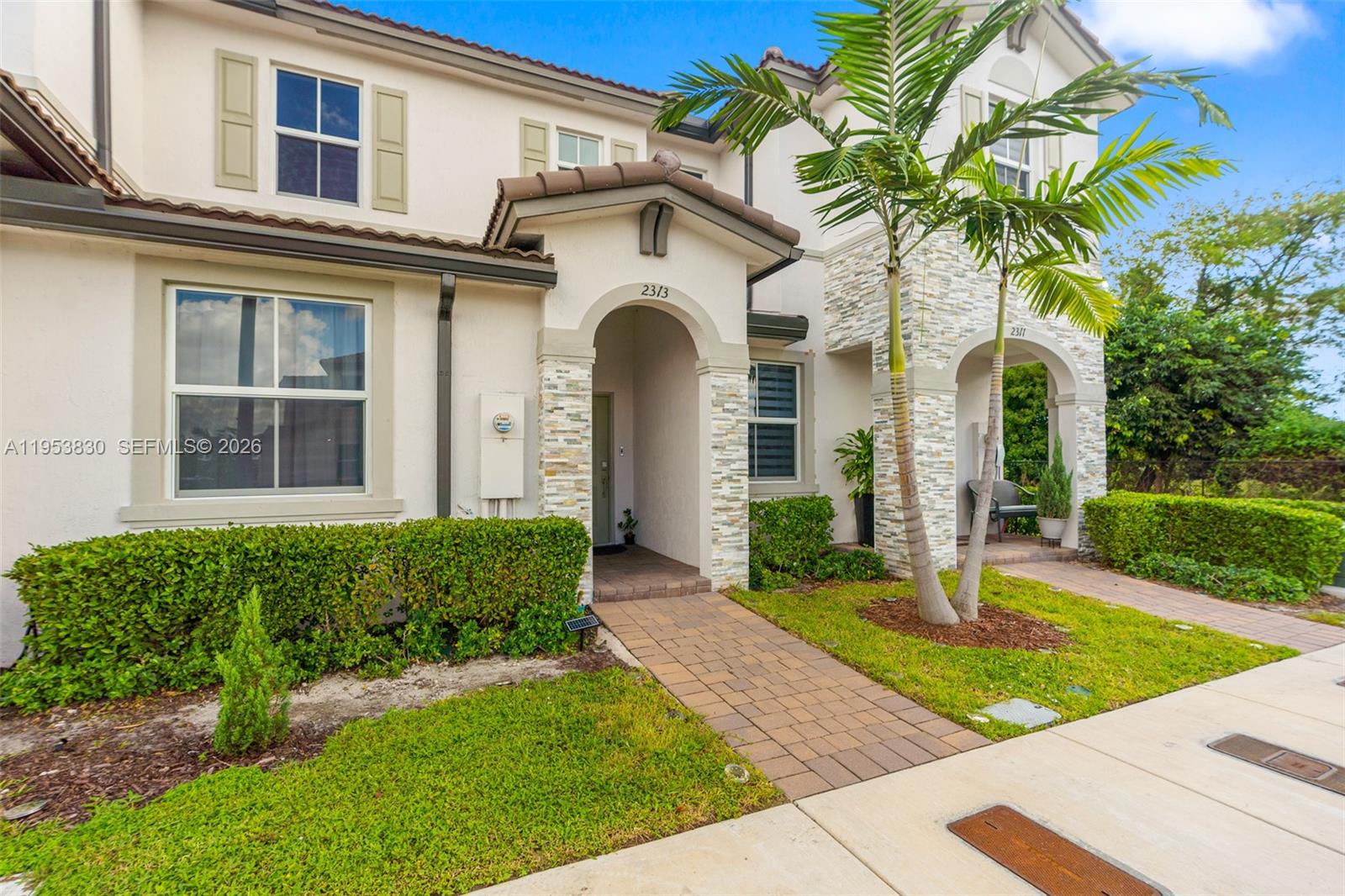 The exterior of a two-story townhouse features stone accents, arched entryways, and a palm tree — 2313 NW 122nd Ter, Miami FL 33167, MIAMI, FL