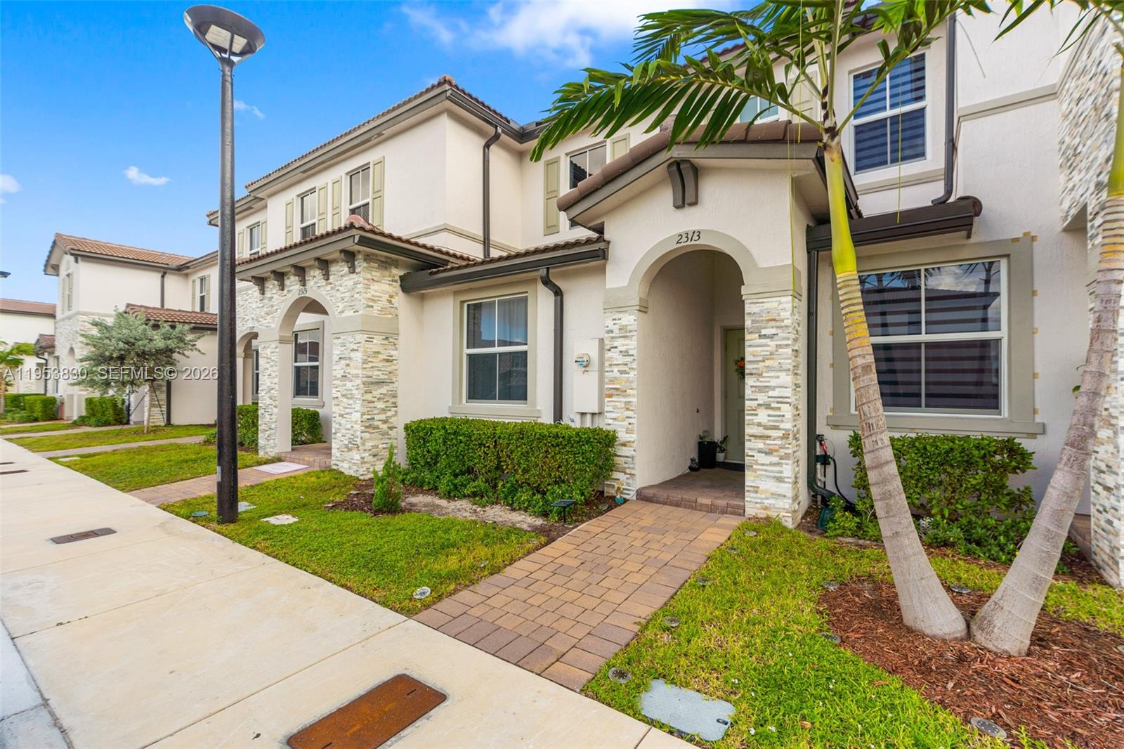 A two-story townhouse exterior features a stone-accented entryway, a brick walkway, and a palm tree — 2313 NW 122nd Ter, Miami FL 33167, MIAMI, FL