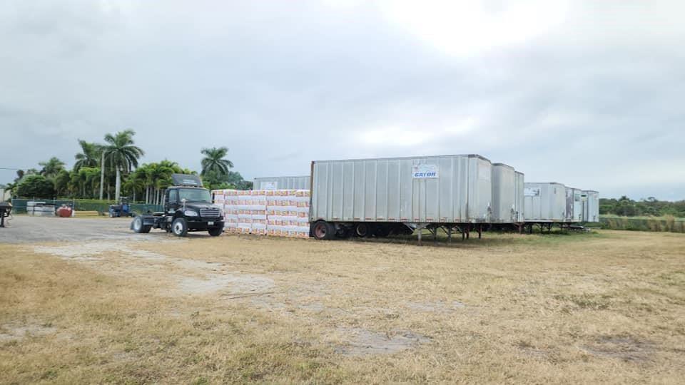 A black semi-truck is parked next to several shipping containers and stacked pallets in a field — 0 S S. State Road, Boynton Beach FL 33472, BOYNTON BEACH, FL