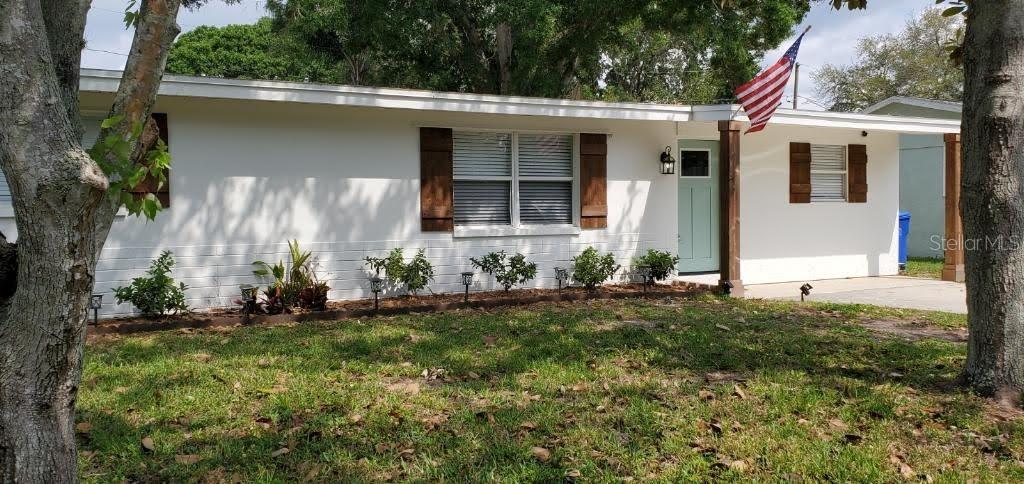 A white single-story house with brown shutters and an American flag near the front door — 1639 ST CATHERINE DRIVE W, DUNEDIN, FL