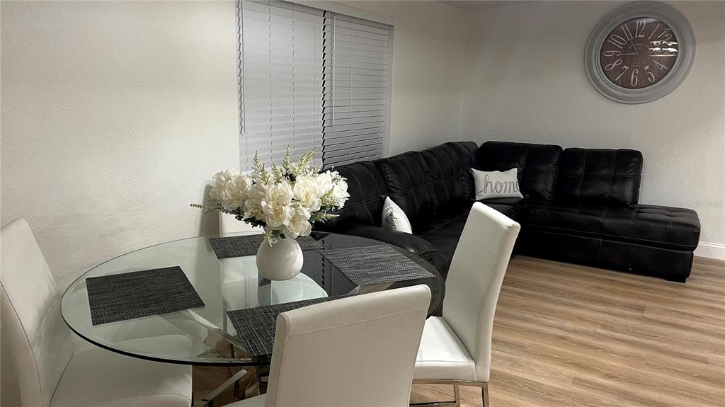 A dining area with a glass table and white chairs sits beside a black sectional sofa — 1639 ST CATHERINE DRIVE W, DUNEDIN, FL