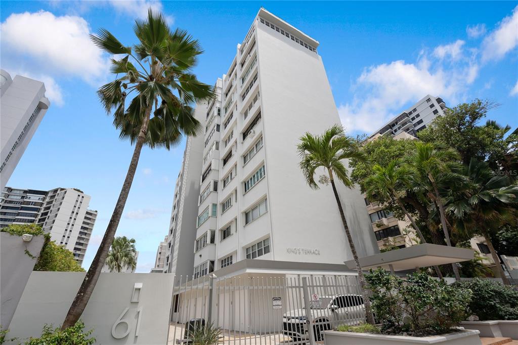 A low-angle view of a white multi-story apartment building with palm trees and fencing — 61 KINGS COURT UNIT 5E, SAN JUAN, PR