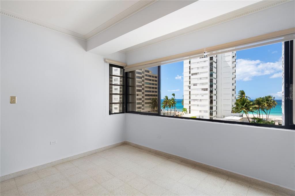 An empty room with white walls, tile flooring, and a large window overlooking the ocean — 61 KINGS COURT UNIT 5E, SAN JUAN, PR