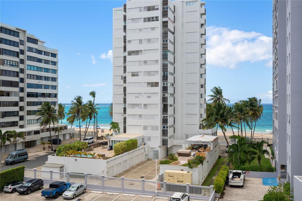 An exterior view of a tall beachfront apartment building with a parking lot and pool — 61 KINGS COURT UNIT 5E, SAN JUAN, PR
