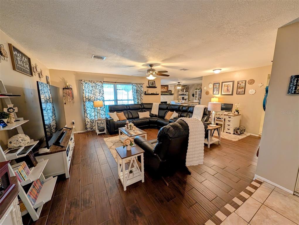 A living room features dark wood-look tile flooring, a large black sectional, and a television — 8240 PENWOOD DRIVE, PORT RICHEY, FL