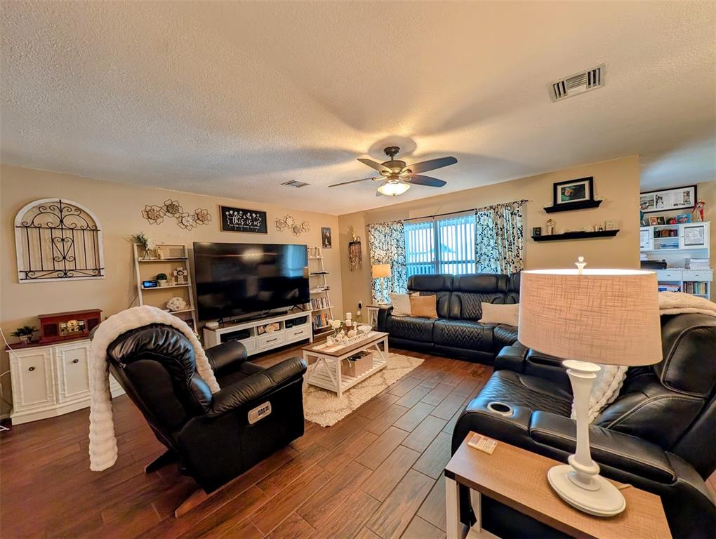 A living room features dark leather furniture, wood-look tile flooring, and a large television — 8240 PENWOOD DRIVE, PORT RICHEY, FL