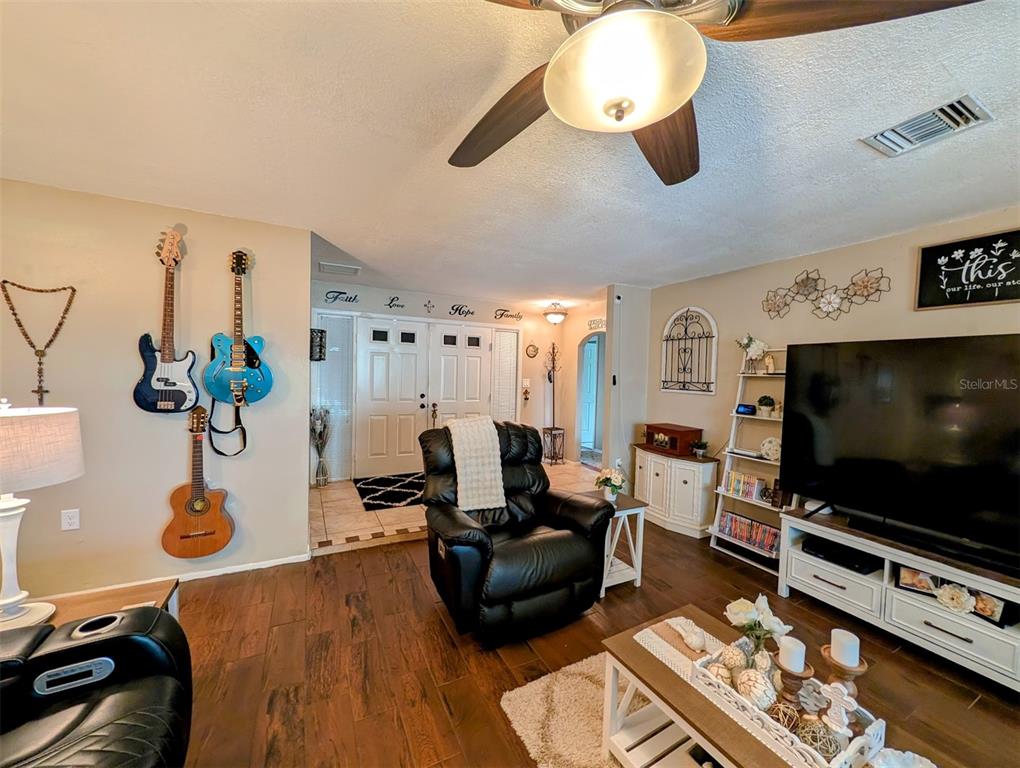 A living room features a black recliner, a large television, and guitars mounted on the wall — 8240 PENWOOD DRIVE, PORT RICHEY, FL