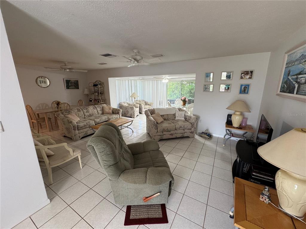 A spacious living room with tile flooring, multiple seating areas, and large sliding glass doors — 239 HAMMOCK TERRACE, VENICE, FL