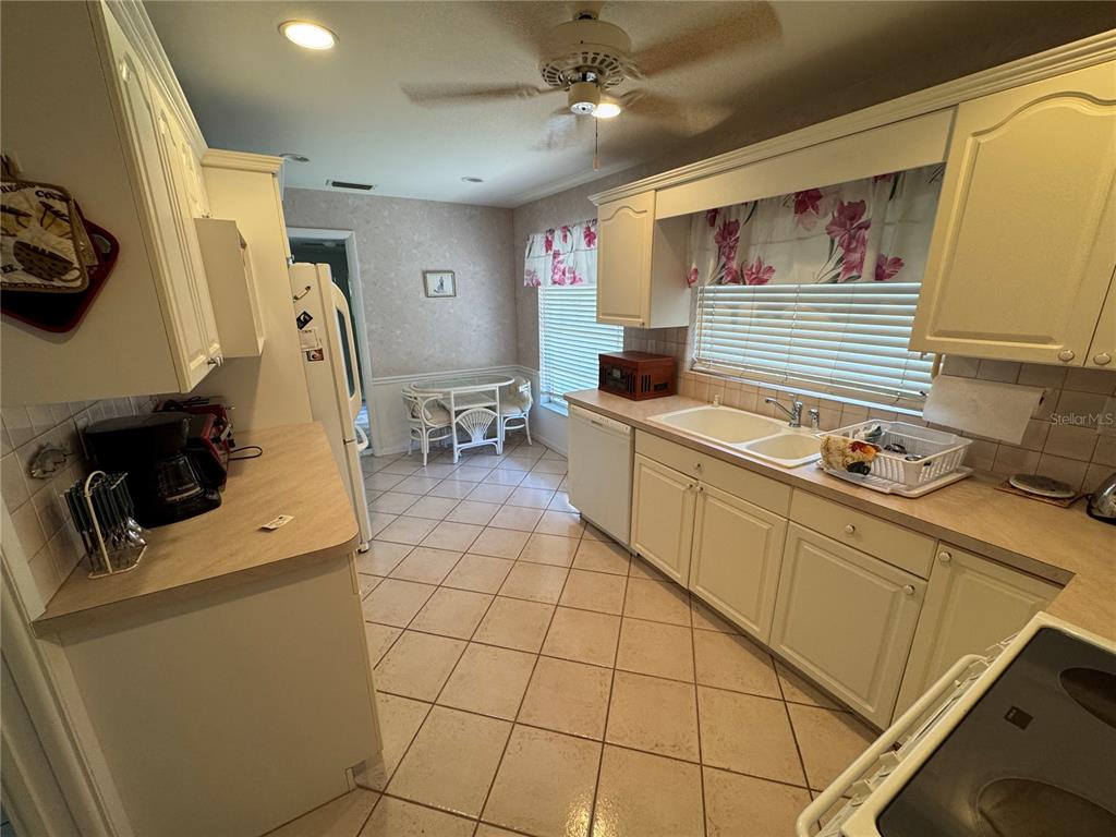 A kitchen features white cabinets, laminate countertops, tile flooring, and a small dining area — 239 HAMMOCK TERRACE, VENICE, FL