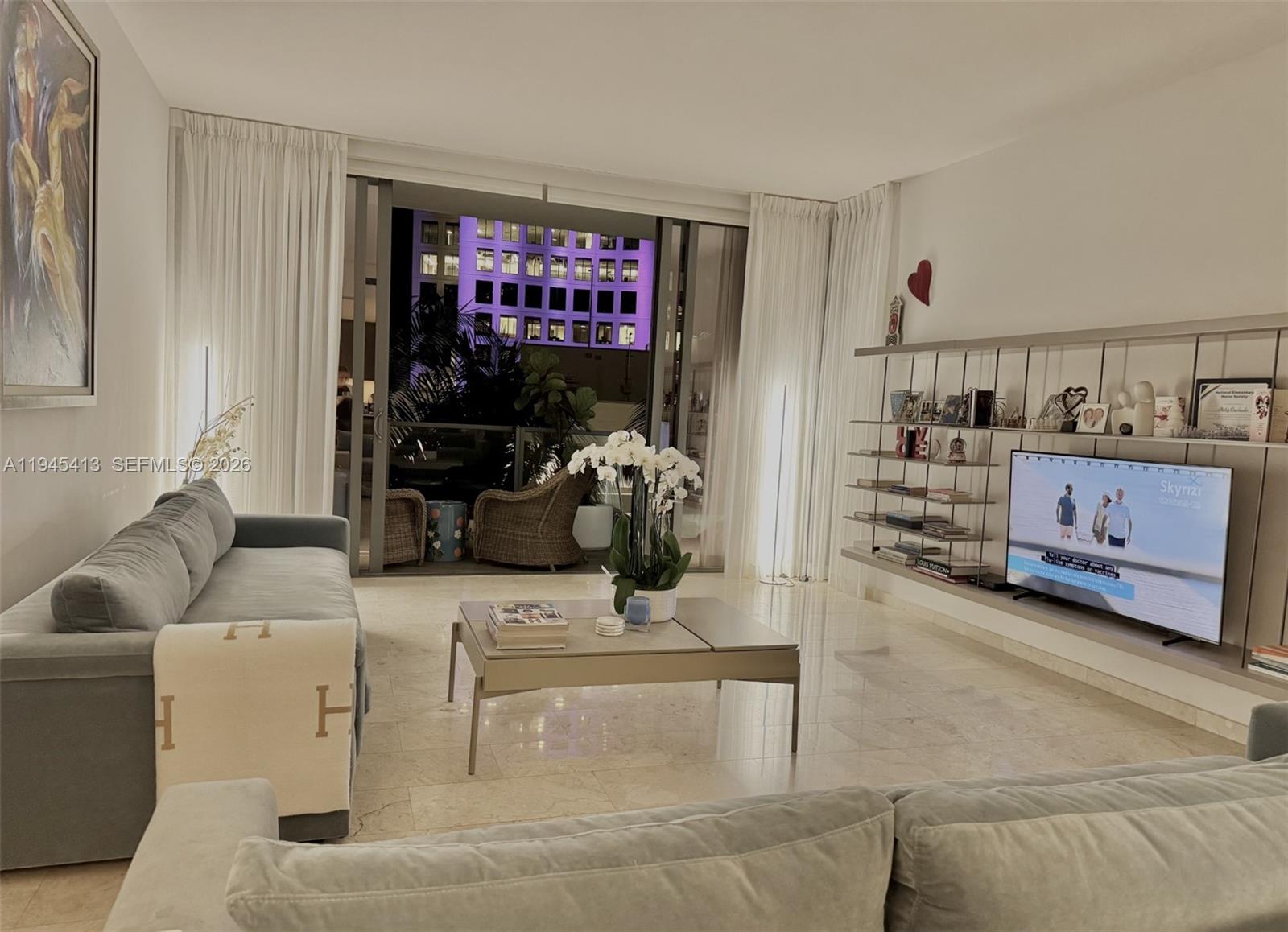 A modern living room features a grey sofa, a coffee table, and a wall-mounted television — 68 SE 6th St # 903, Miami FL 33131, MIAMI, FL