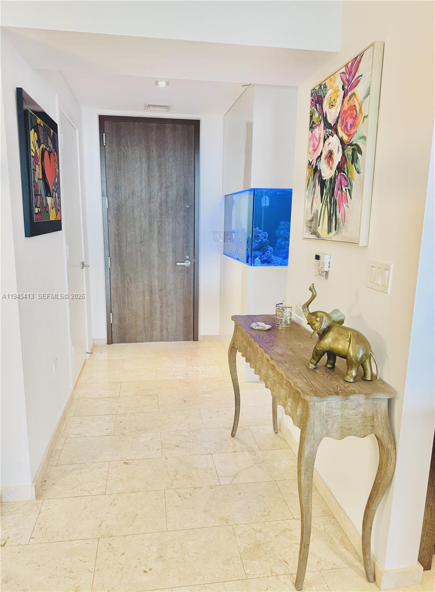 A hallway features a wooden door, a console table with an elephant statue, and an aquarium — 68 SE 6th St # 903, Miami FL 33131, MIAMI, FL