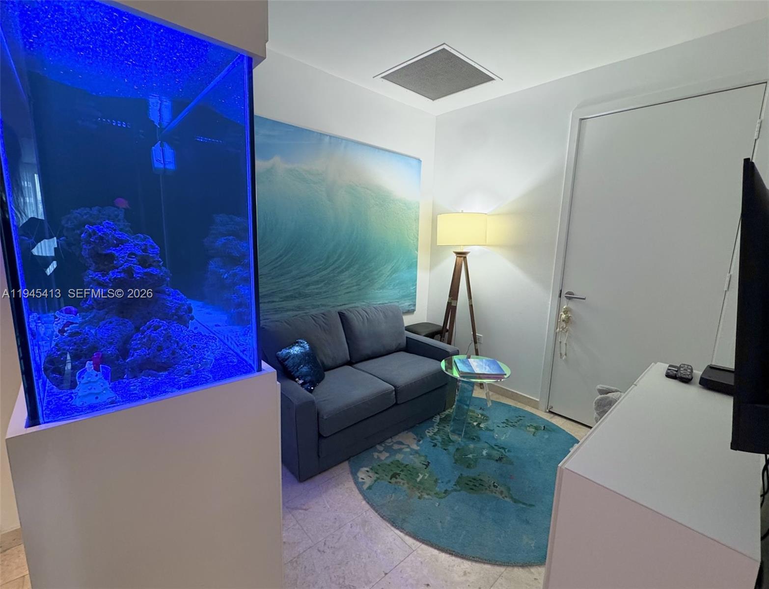 A small room features a large aquarium, a blue sofa, and a world map rug — 68 SE 6th St # 903, Miami FL 33131, MIAMI, FL