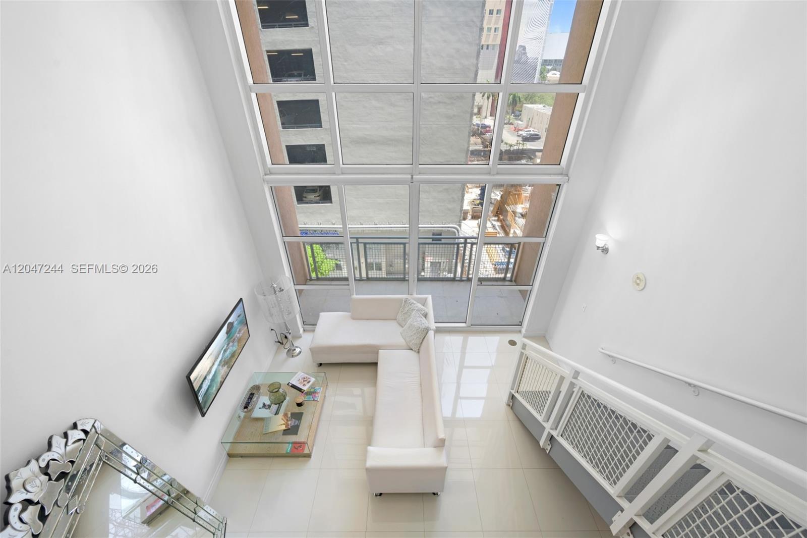 A high-angle view of a modern living room with a double-height window and balcony — 244 Biscayne Blvd # 451, Miami FL 33132, MIAMI, FL