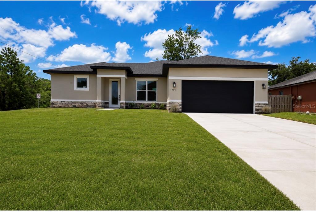 A single-story house with a beige stucco exterior, stone accents, and a black garage door — 701 FULMAR COURT, POINCIANA, FL