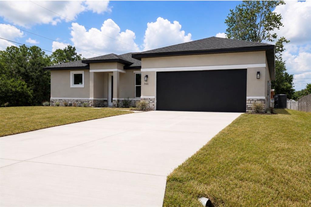 A single-story house with a beige stucco exterior, a black garage door, and a concrete driveway — 701 FULMAR COURT, POINCIANA, FL