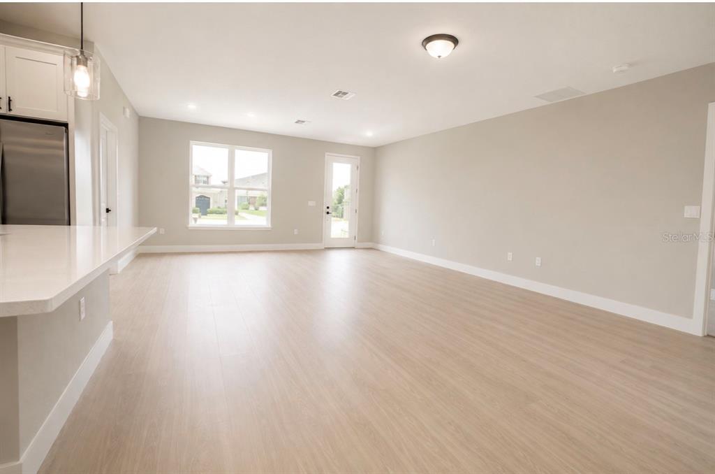 An open-concept room features light wood-look flooring, neutral walls, a kitchen island, and glass doors — 701 FULMAR COURT, POINCIANA, FL