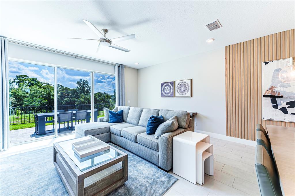 A living room features a grey sectional sofa, a glass coffee table, and wood-slat wall paneling — 7917 NW SPECTRUM DRIVE, KISSIMMEE, FL