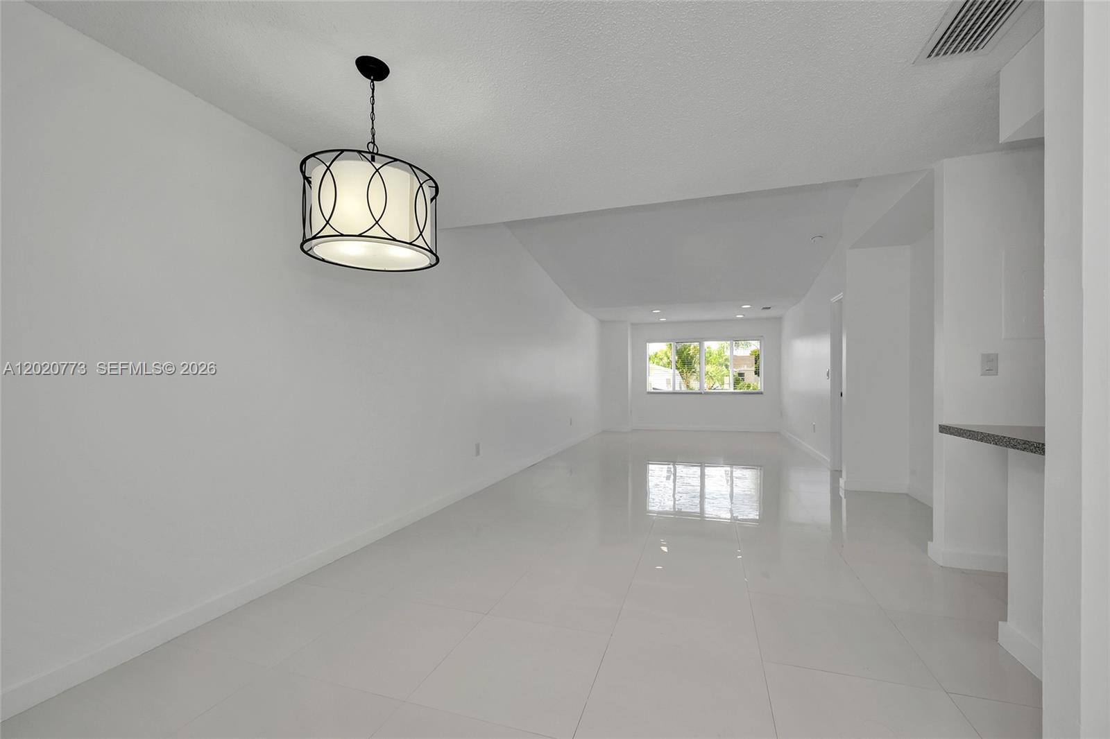 A bright, empty room features white walls, glossy tile flooring, and a modern drum chandelier — 6720 NW 174th Ter # 18, Hialeah FL 33015, HIALEAH, FL