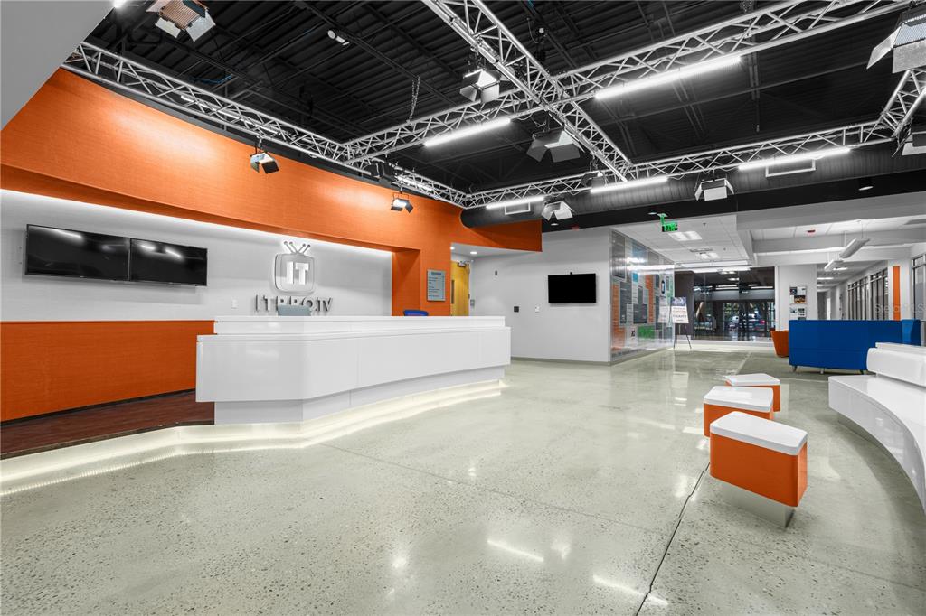 A modern office lobby features a white reception desk, orange accent walls, and industrial lighting — 7525 NW 4TH BOULEVARD, GAINESVILLE, FL