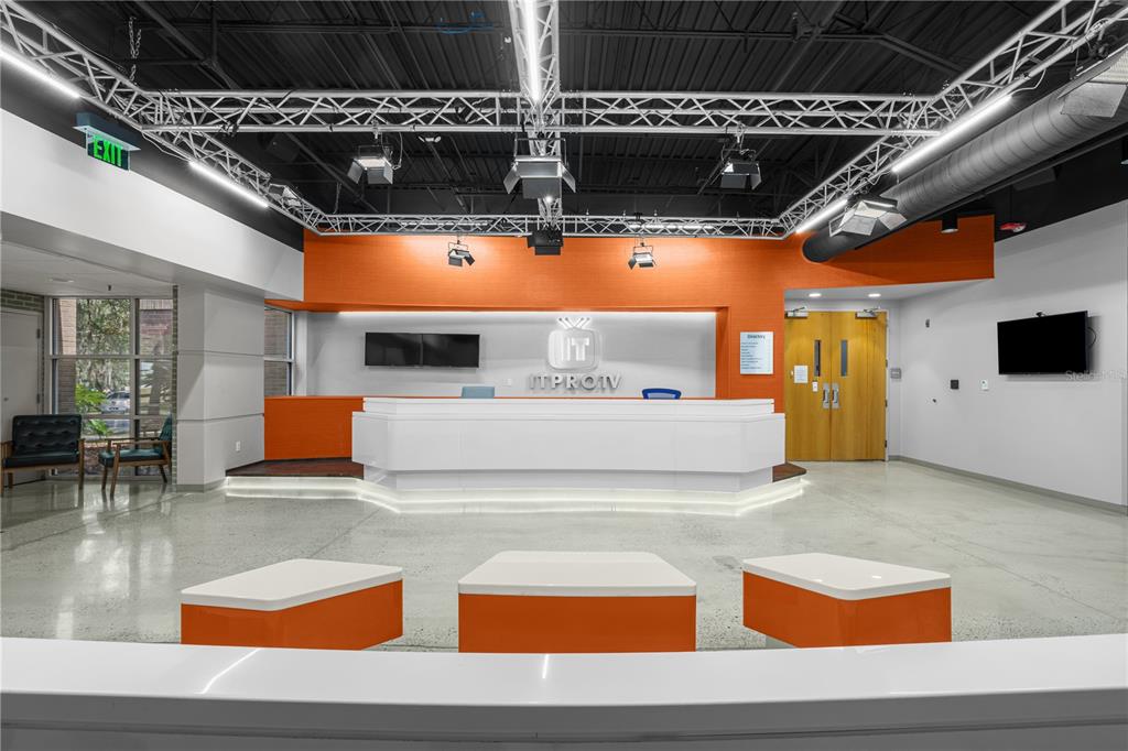 A modern office reception area features a white desk, orange accents, and exposed ceiling trusses — 7525 NW 4TH BOULEVARD, GAINESVILLE, FL