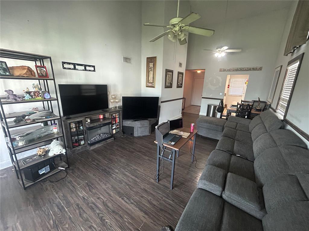 A living room features a large gray sectional sofa, two televisions, and dark wood flooring — 6519 W NEWBERRY ROAD UNIT 309, GAINESVILLE, FL