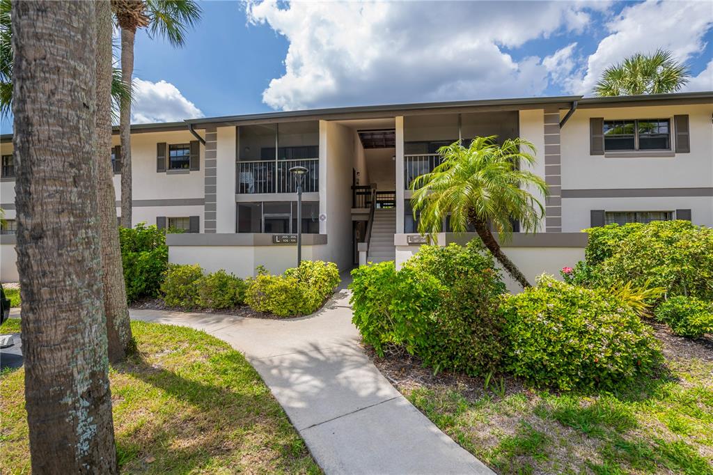 A concrete walkway leads to the entrance of a two-story apartment building with balconies — 1515 FORREST NELSON BOULEVARD UNIT L105, PORT CHARLOTTE, FL