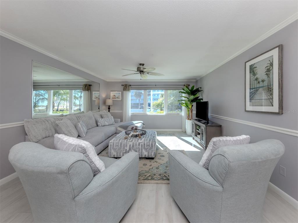 A living room features light gray walls, a sectional sofa, two armchairs, and a patterned ottoman — 500 THE ESPLANADE N UNIT 102, VENICE, FL