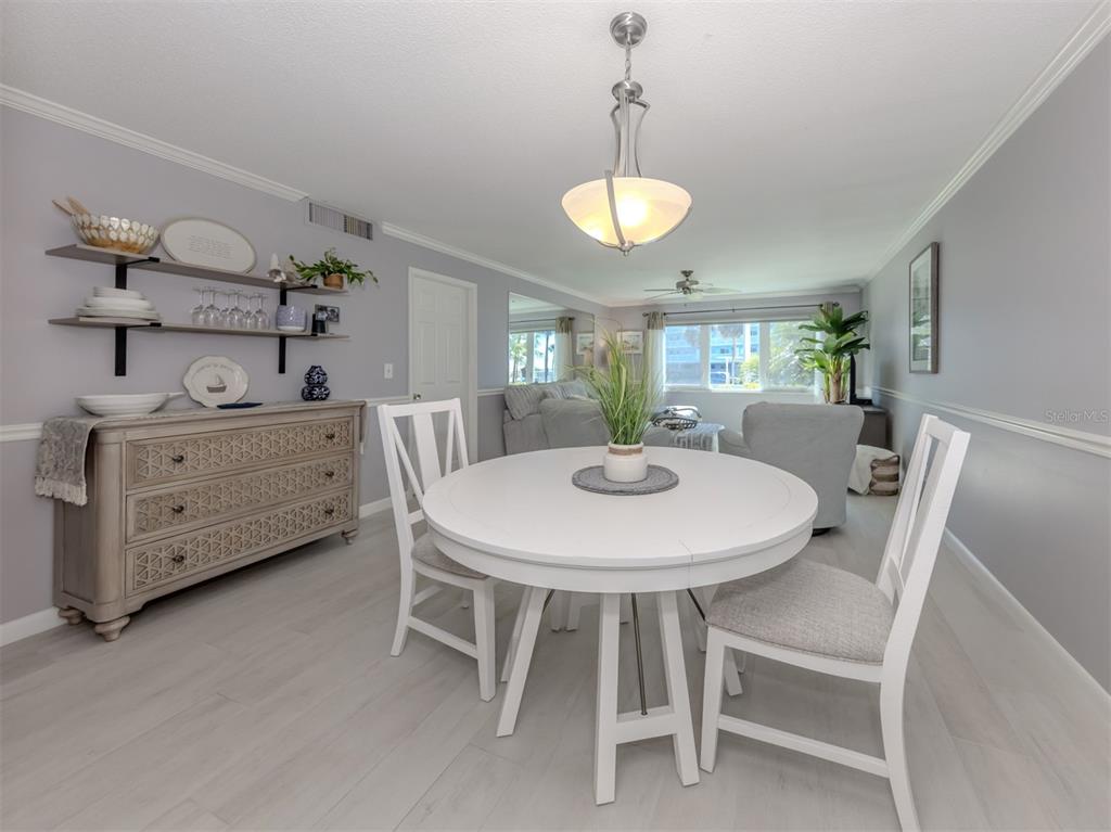 A dining area features a white round table, two chairs, and a wooden sideboard — 500 THE ESPLANADE N UNIT 102, VENICE, FL