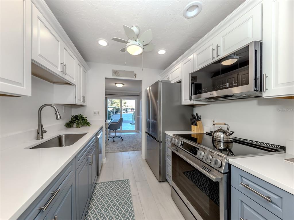 A galley kitchen features white upper cabinets, blue lower cabinets, stainless steel appliances, and tile flooring — 500 THE ESPLANADE N UNIT 102, VENICE, FL