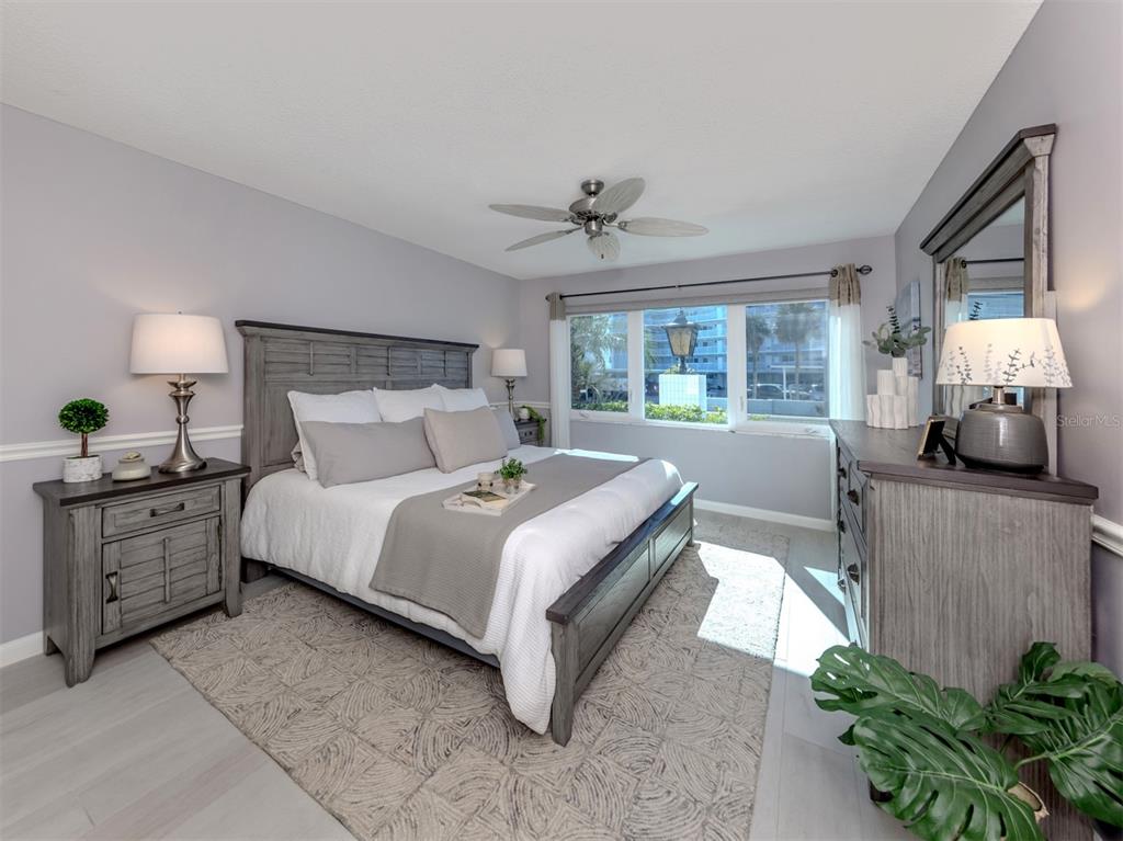 A bedroom features a gray wooden bed frame, matching furniture, and a window with exterior views — 500 THE ESPLANADE N UNIT 102, VENICE, FL