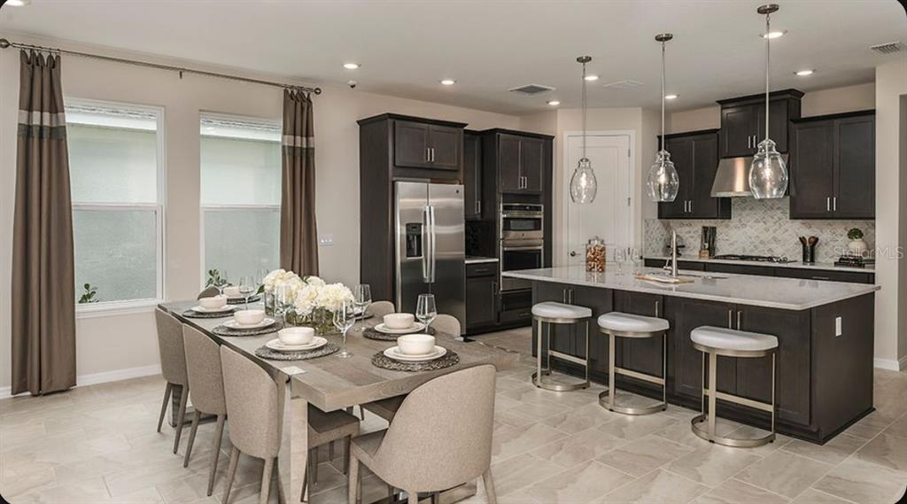 A modern kitchen features white cabinetry, a large central island, and light wood-look flooring — 7028 FOXBORO WAY, NOKOMIS, FL
