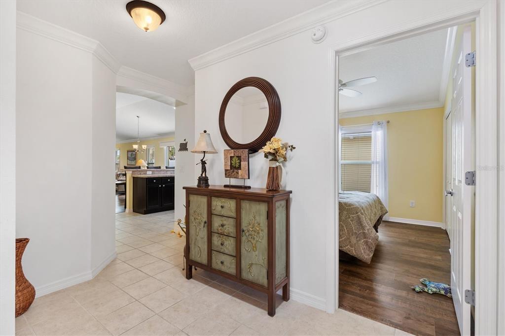 A tiled entryway features a decorative cabinet, a round mirror, and a doorway to a bedroom — 3025 BARTOW LANE, THE VILLAGES, FL