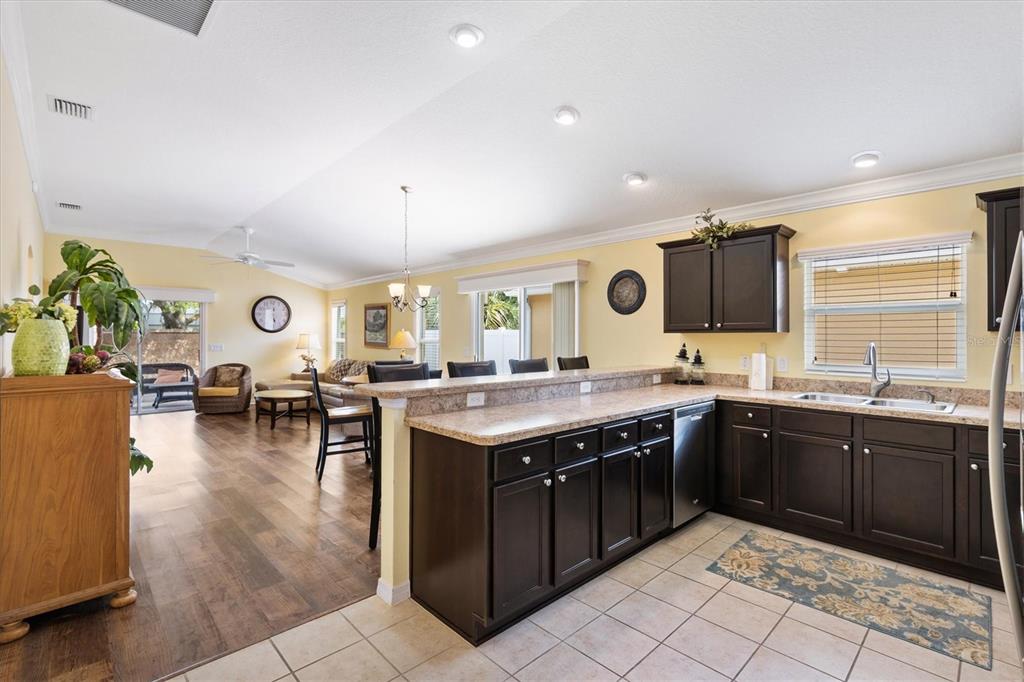 A kitchen with dark wood cabinets and granite countertops overlooks an open-concept living area — 3025 BARTOW LANE, THE VILLAGES, FL