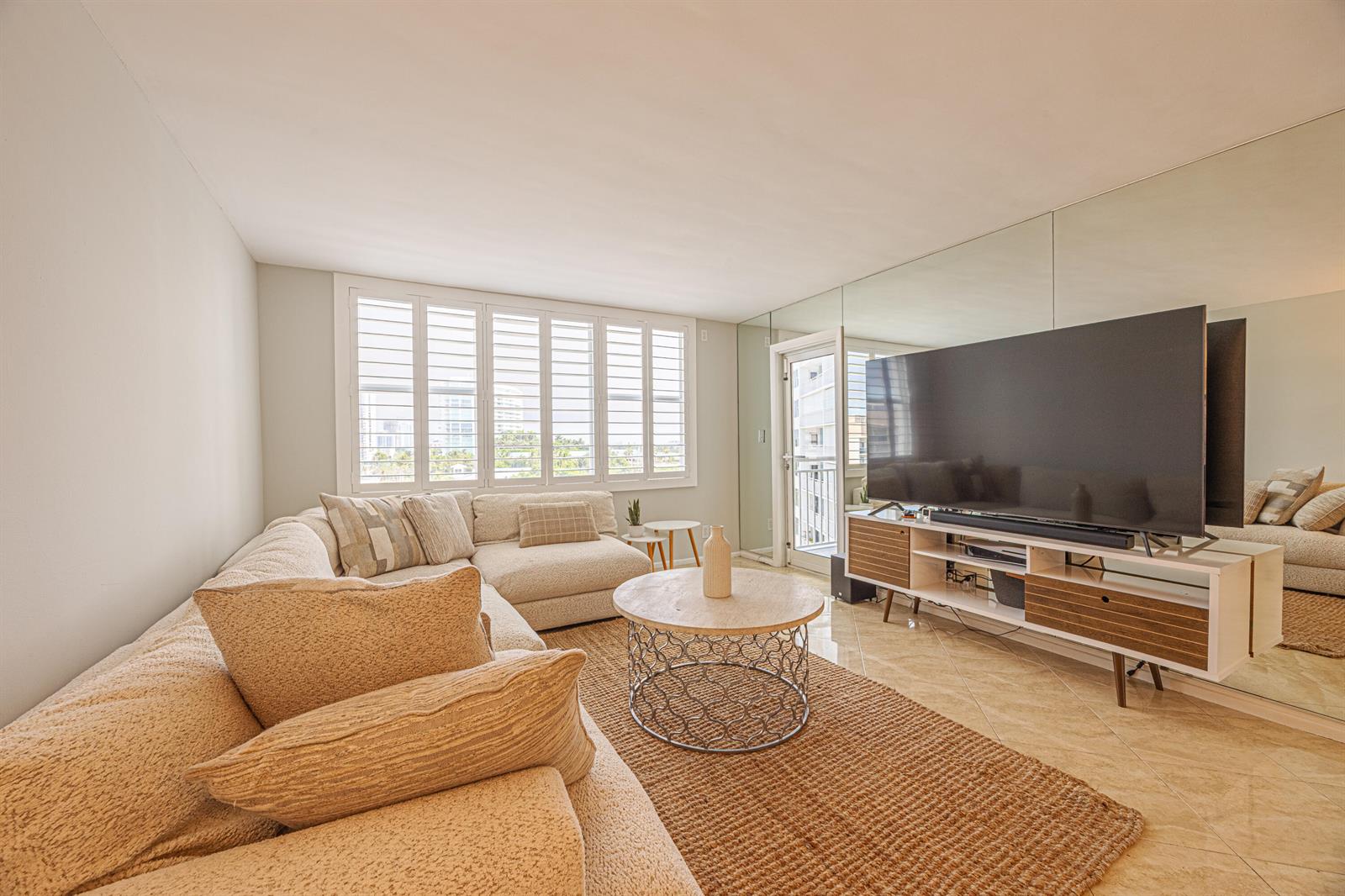 A living room features a large sectional sofa, a round coffee table, and a television console — 201 N Ocean Boulevard # 702, Pompano Beach FL 33062, POMPANO BEACH, FL