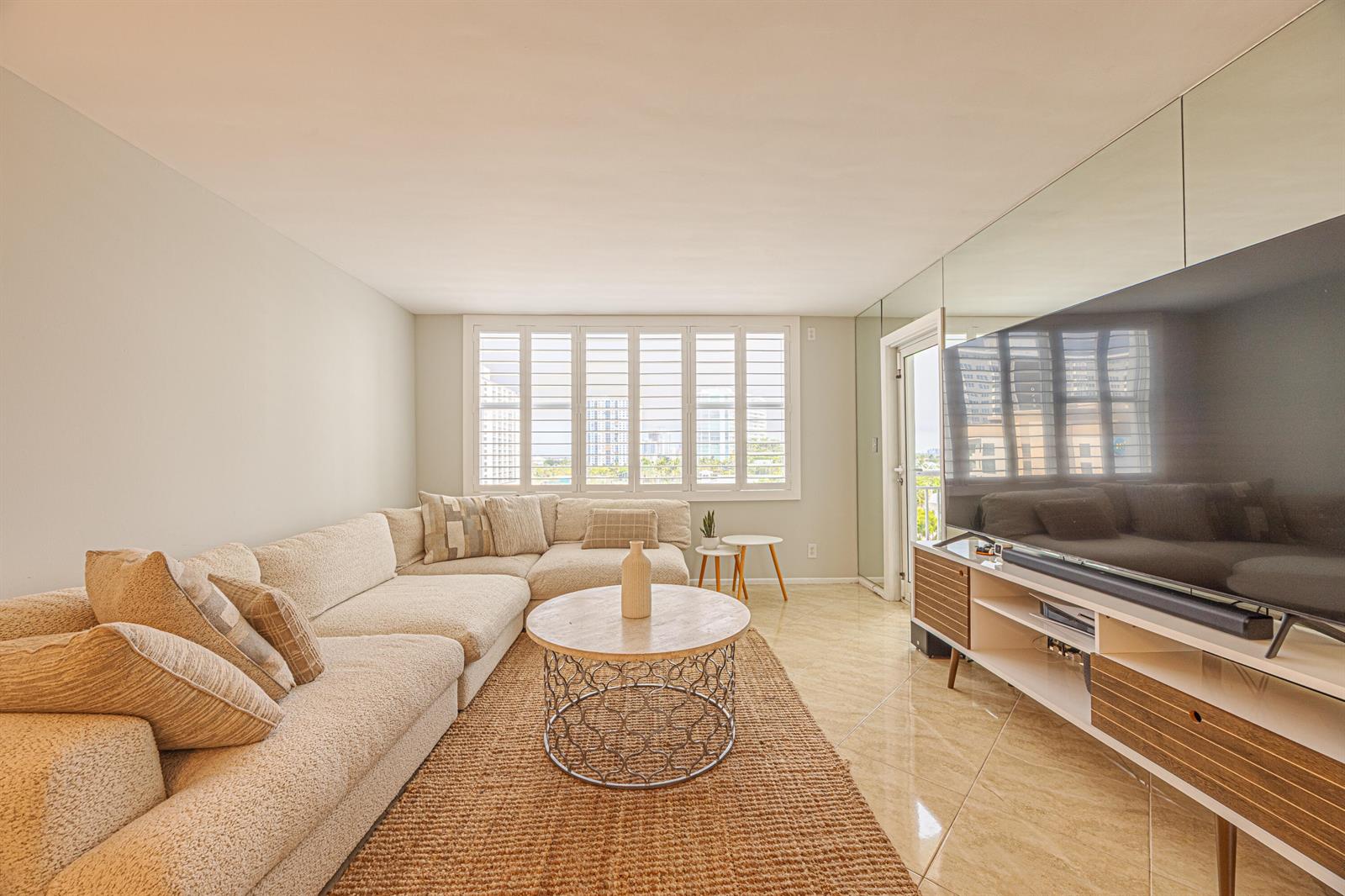 A living room features a large sectional sofa, a round coffee table, and a television — 201 N Ocean Boulevard # 702, Pompano Beach FL 33062, POMPANO BEACH, FL