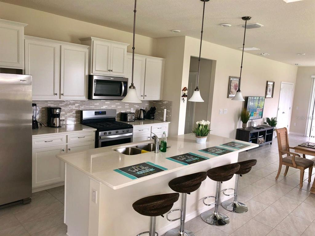 A kitchen features white cabinets, stainless steel appliances, a quartz island, and three bar stools — 5465 MISTY OAK CIRCLE, DAVENPORT, FL