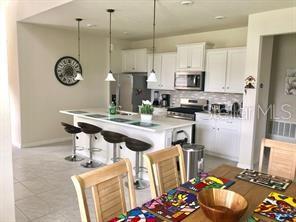 A kitchen with white cabinets, a central island with bar seating, and a dining area — 5465 MISTY OAK CIRCLE, DAVENPORT, FL