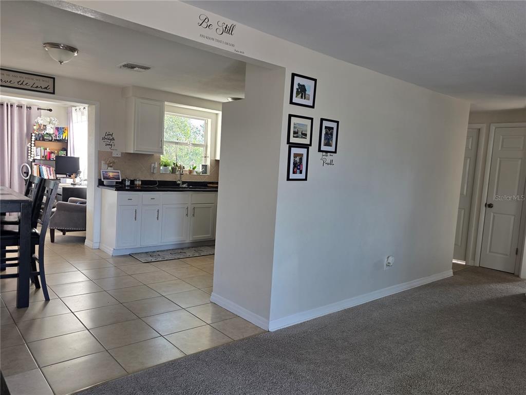 A view from a carpeted living area looking into a kitchen with white cabinets — 4823 LONGWOOD AVENUE, HOLIDAY, FL