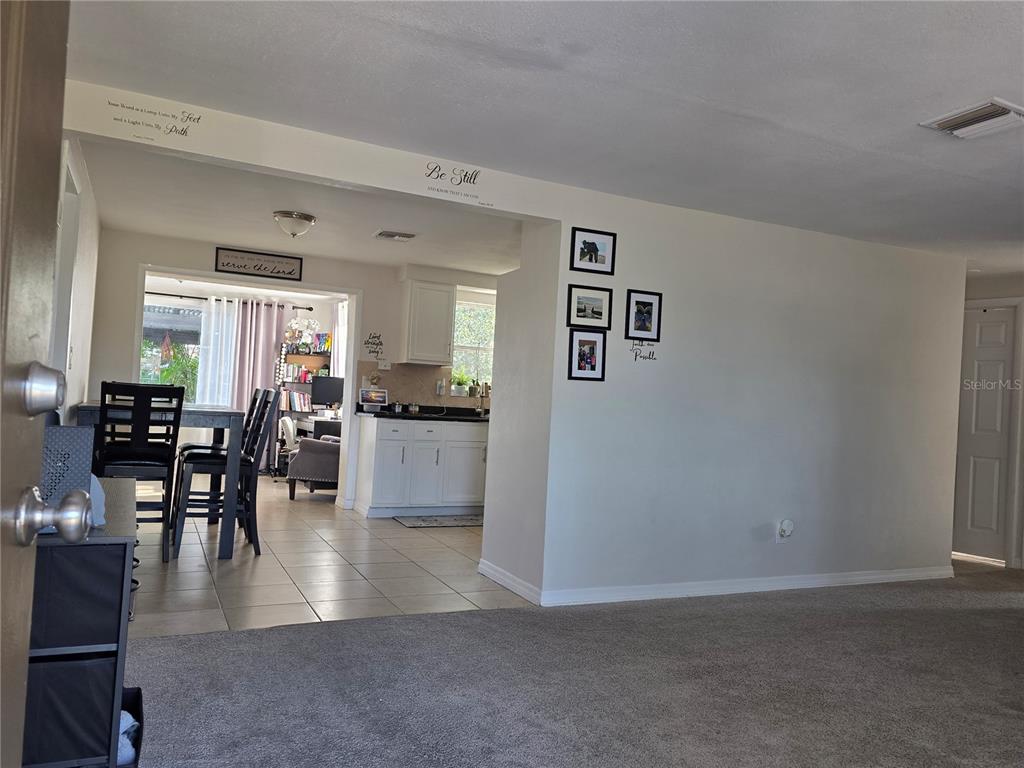 A view from a carpeted living room looking into a tiled dining area and kitchen — 4823 LONGWOOD AVENUE, HOLIDAY, FL