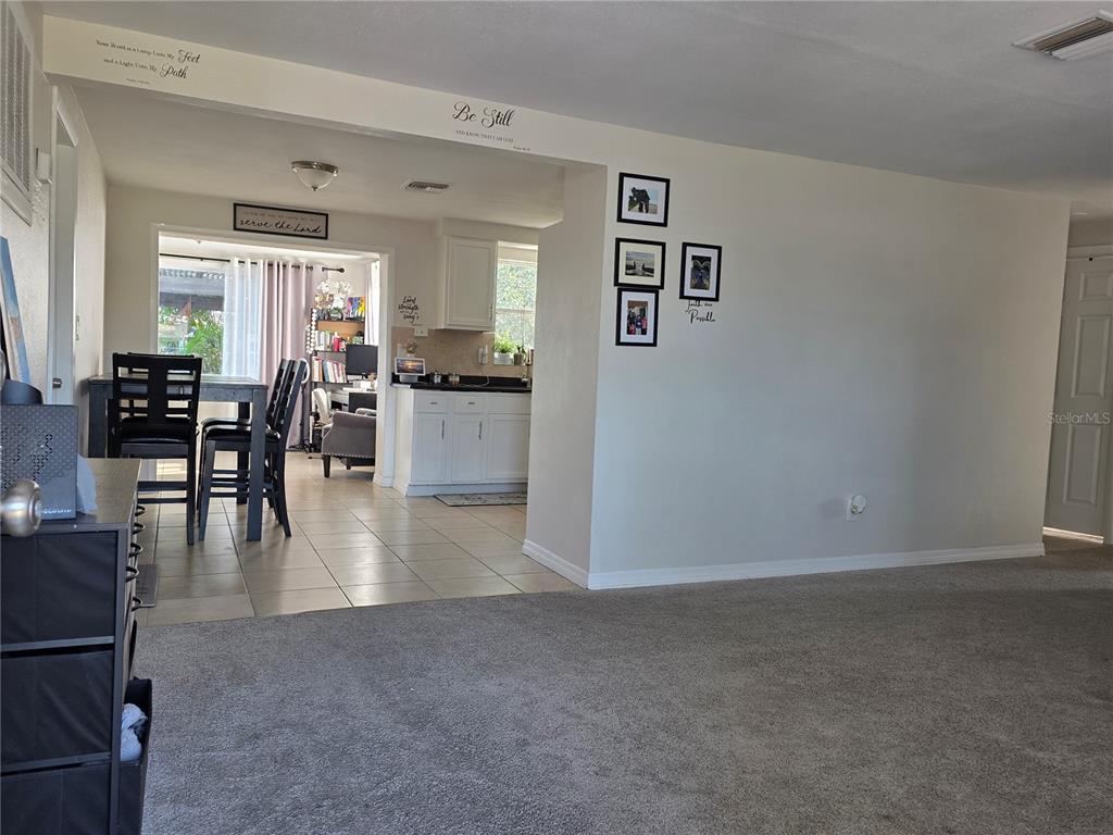 A carpeted living room opens into a tiled dining area and kitchen with white cabinets — 4823 LONGWOOD AVENUE, HOLIDAY, FL