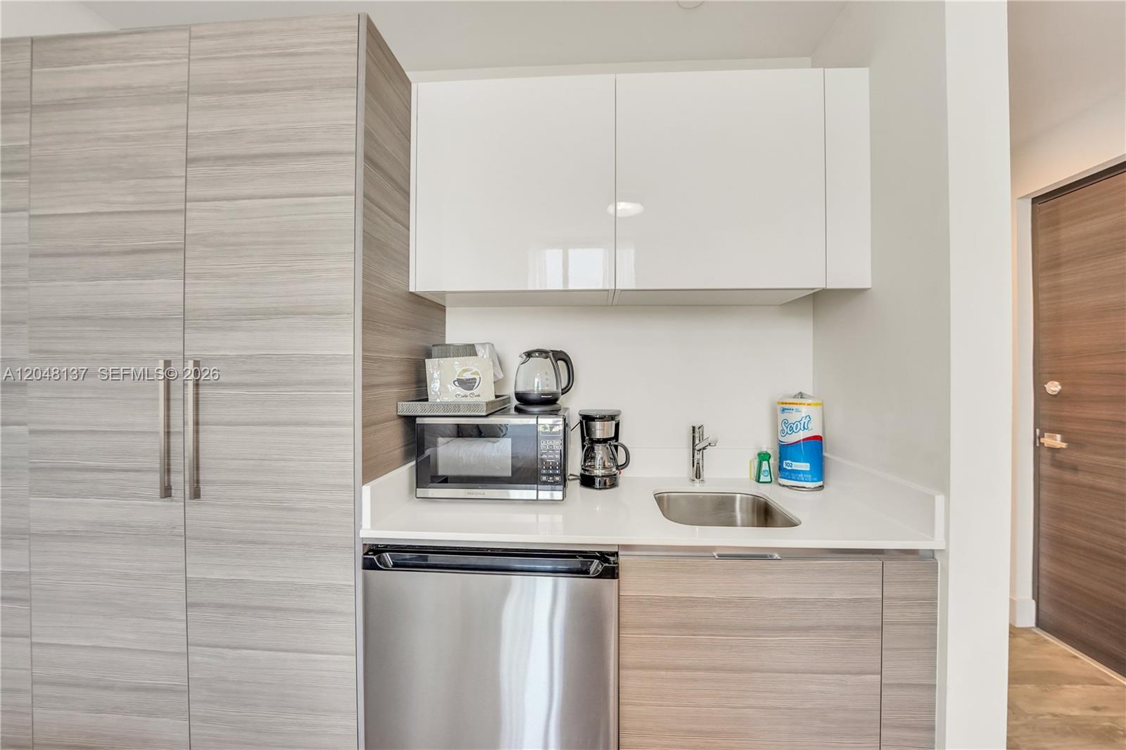 A kitchenette features wood-grain cabinetry, a white countertop, a stainless steel sink, and a microwave — 777 N Ocean Dr # S314, Hollywood FL 33019, HOLLYWOOD, FL