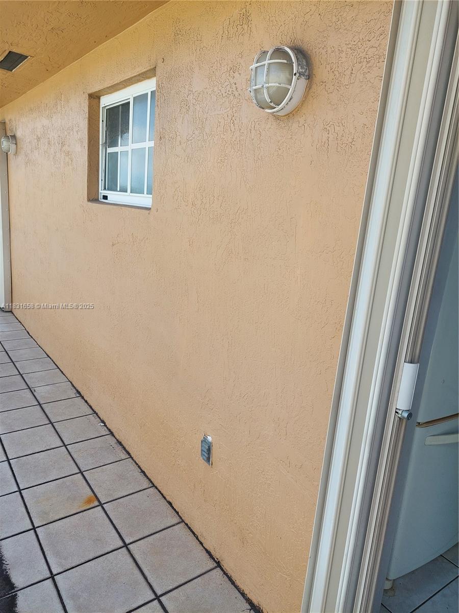 A beige stucco exterior wall features a window, a light fixture, and tiled flooring — 2403 W 76th St # 203, Hialeah FL 33016, HIALEAH, FL