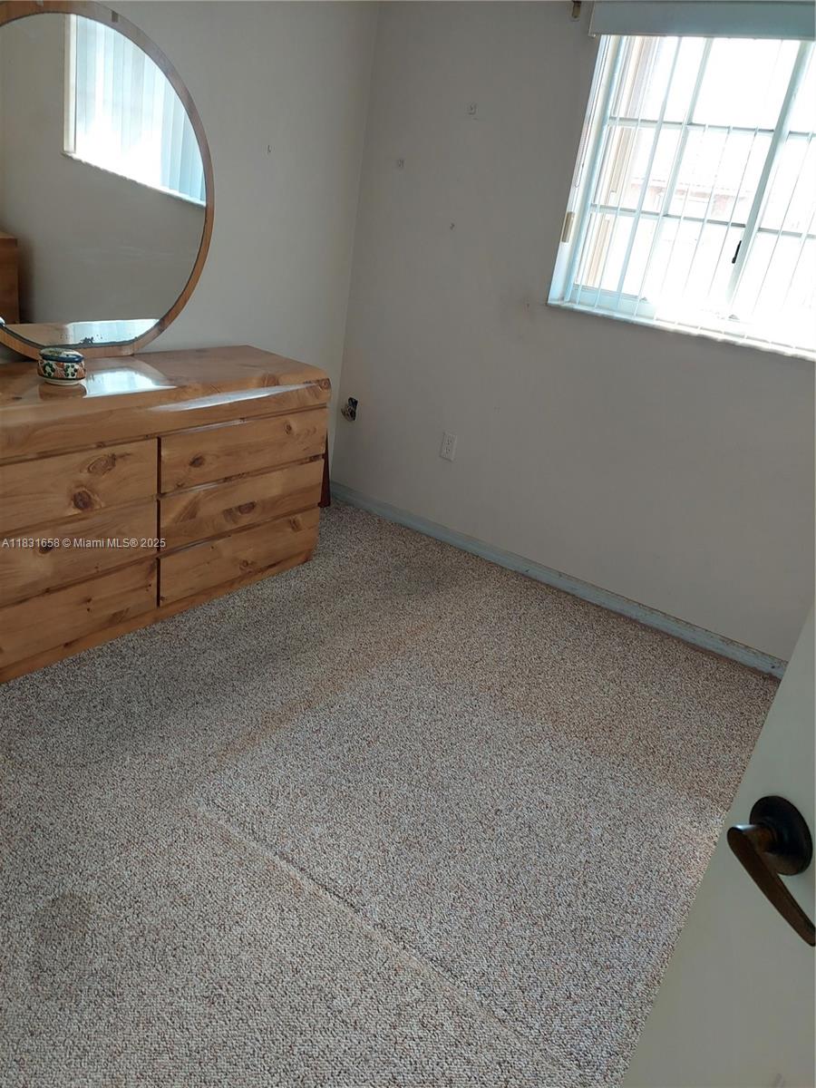 A bedroom features beige carpet, a wooden dresser with a round mirror, and a window — 2403 W 76th St # 203, Hialeah FL 33016, HIALEAH, FL