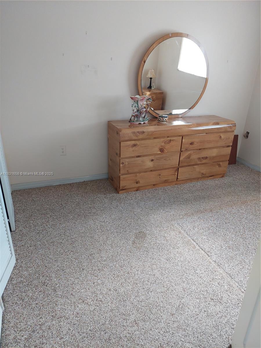 A bedroom features a wooden dresser with a round mirror on a carpeted floor — 2403 W 76th St # 203, Hialeah FL 33016, HIALEAH, FL