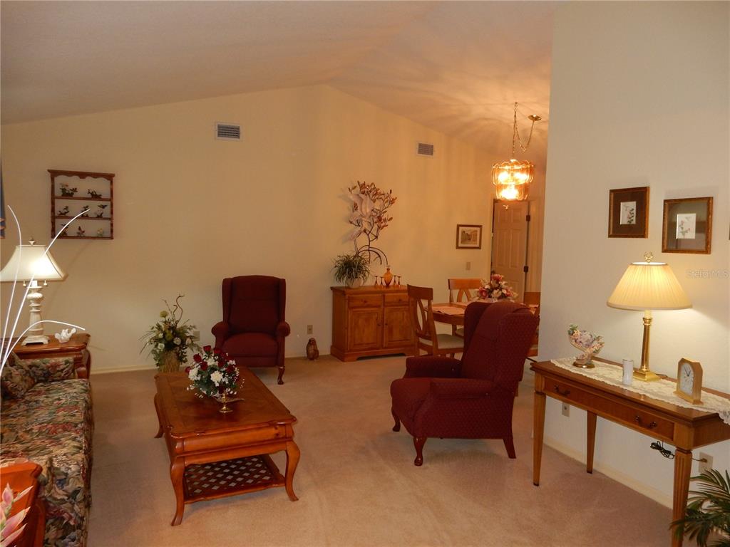 A living room with beige carpet, two armchairs, a coffee table, and a dining area — 21240 CHATBURN AVENUE, PORT CHARLOTTE, FL
