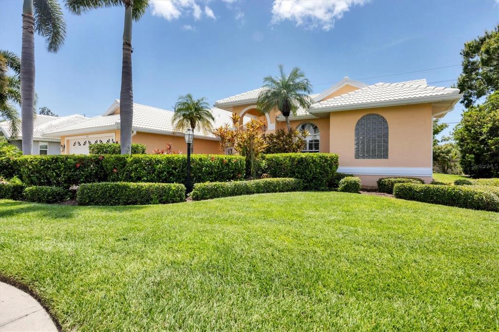 A single-story house with a peach exterior, white tile roof, and a manicured front lawn — 6392 WOODBIRCH PLACE, SARASOTA, FL