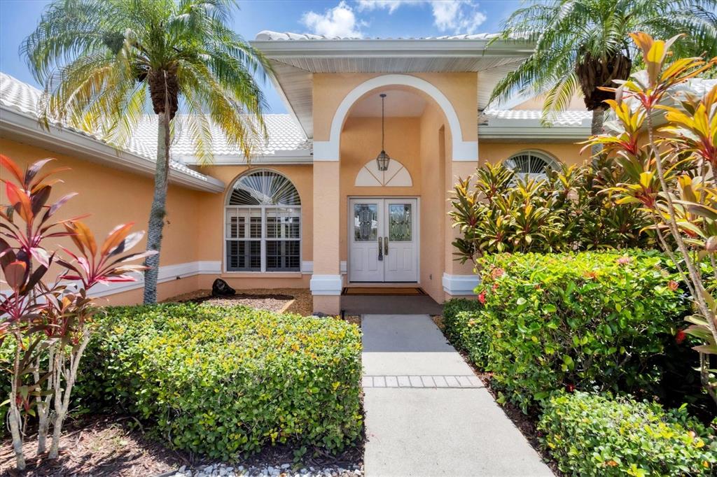 A concrete walkway leads to the double front doors of a peach-colored house with landscaping — 6392 WOODBIRCH PLACE, SARASOTA, FL